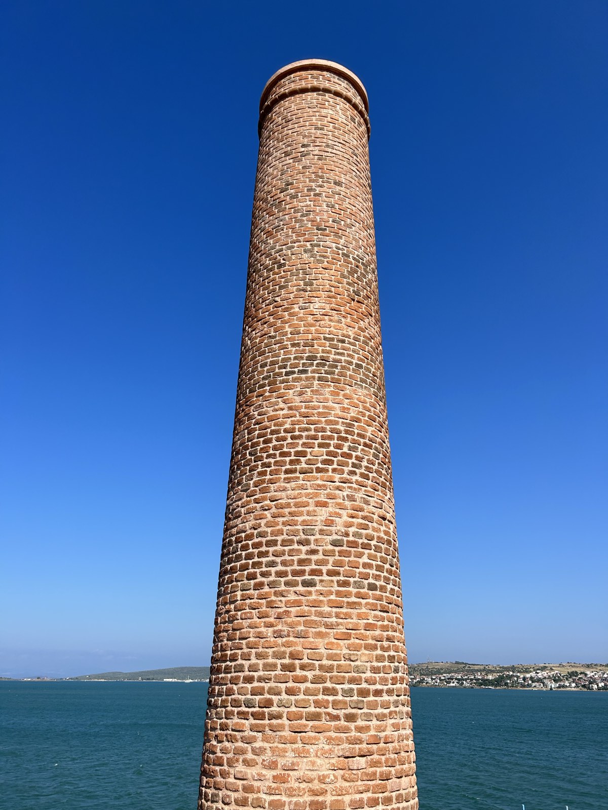 Onarımı tamamlanmış tuğla baca, arkasında deniz ve karşı kıyı