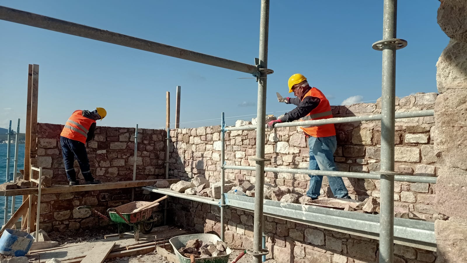 İskele üstünde usta, taş duvarın derzlerini mala ile dolduruyor