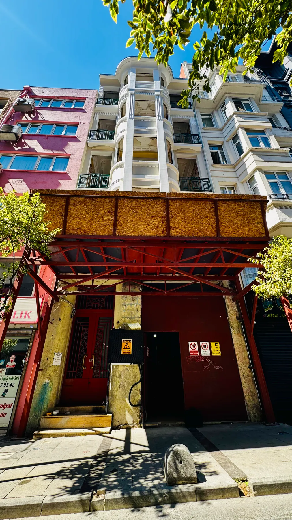 Apartmanın kapalı girişi: kırmızı kapı, uyarı levhaları ve tünelin taşıyıcı ayakları