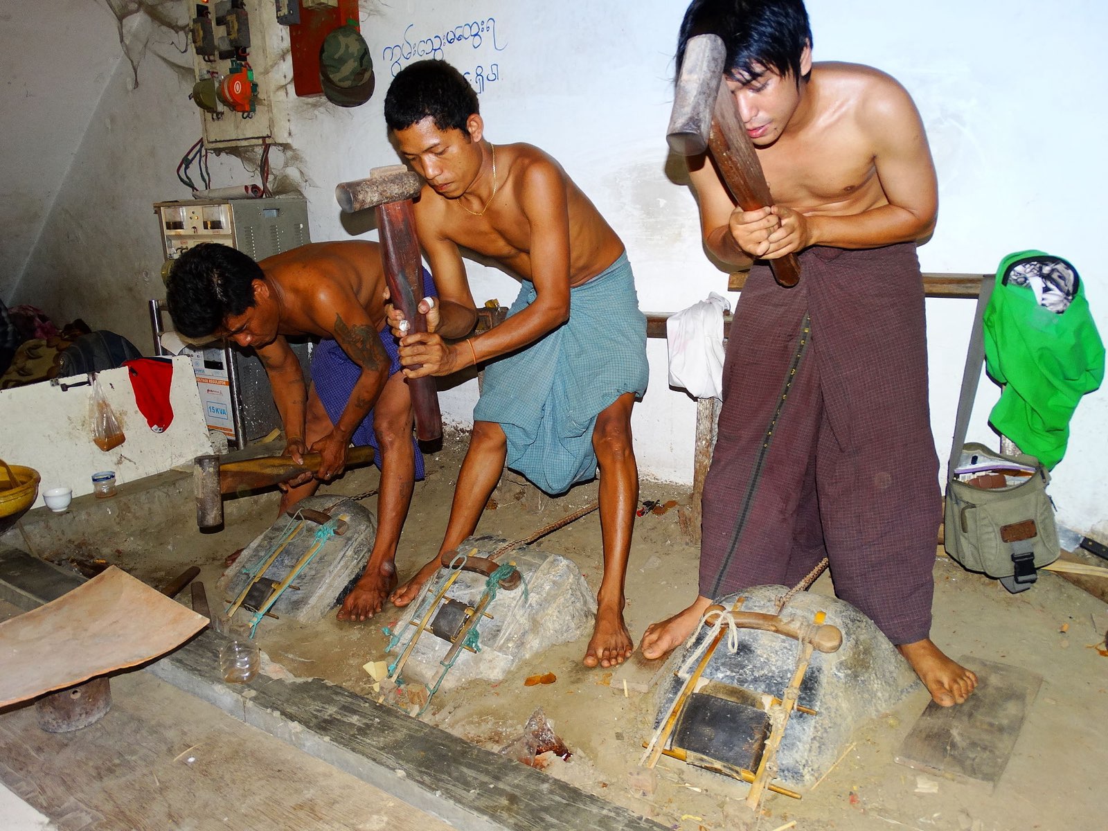 Mandalay'da bir atölyede üç usta, tokmakla altın döverek varak inceltiyor