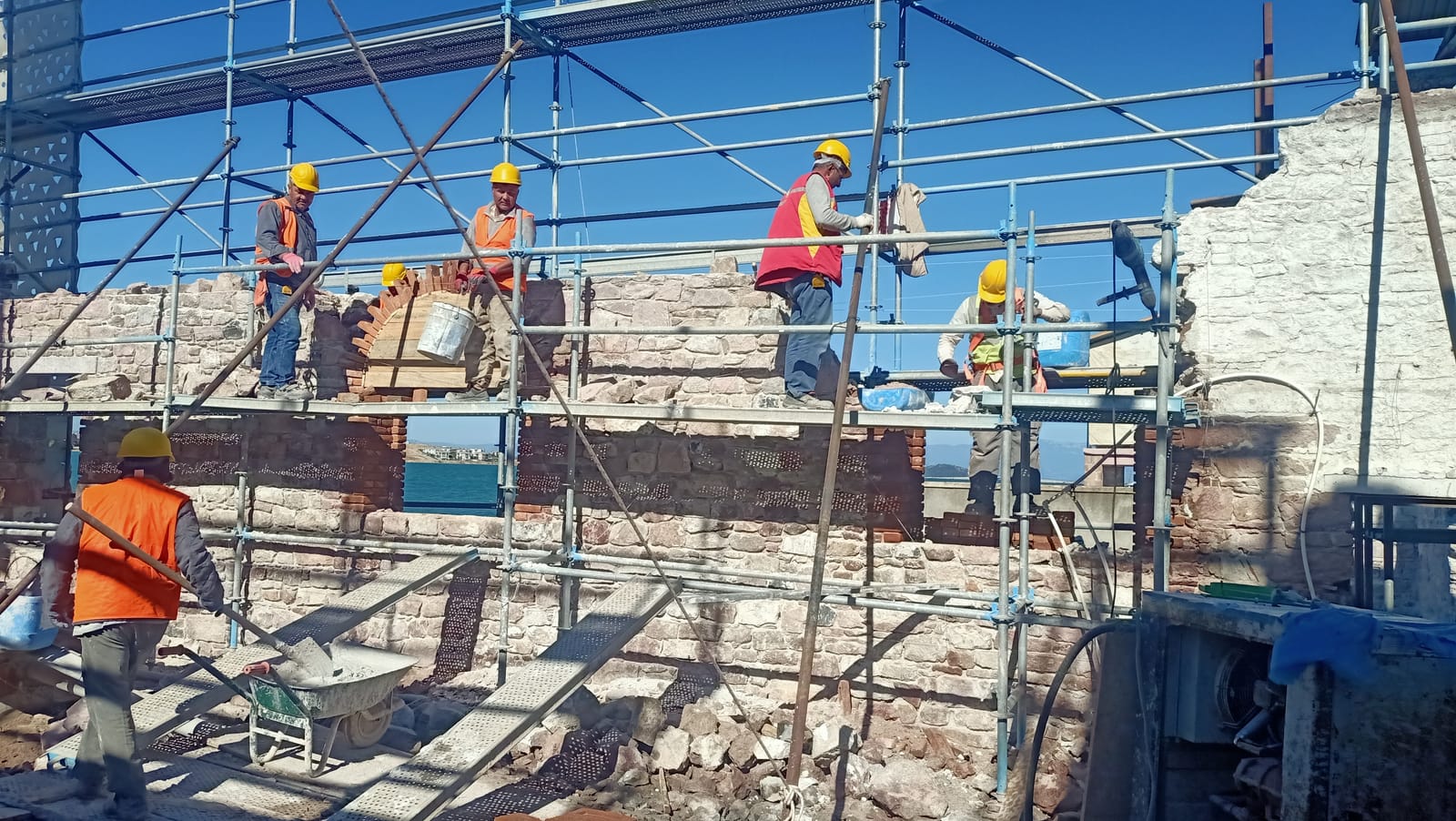 İskele üstünde birkaç usta, taş ve tuğla duvarı birlikte örüyor